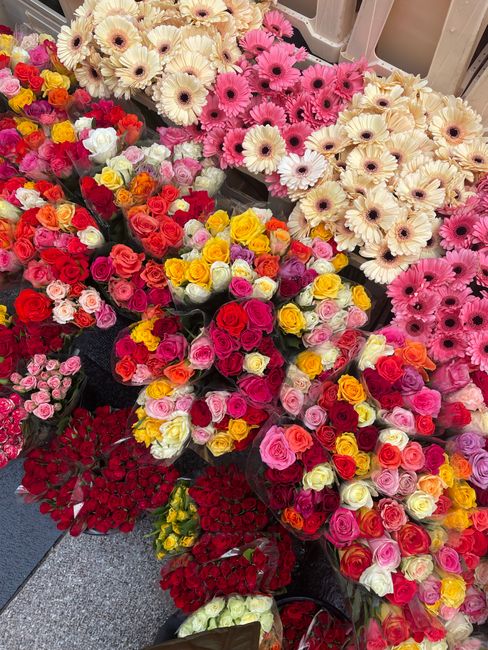 An abundant display of fresh floral bouquets featuring a vibrant mix of roses, gerbera daisies, and other seasonal flowers in shades of pink, red, yellow, and white, arranged in various sizes and styl