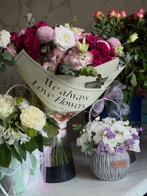 A vibrant bouquet of pink and white roses, complemented by pink and white chrysanthemums, is wrapped in white paper with the phrase 'We always love flowers' printed on it. The arrangement is placed in